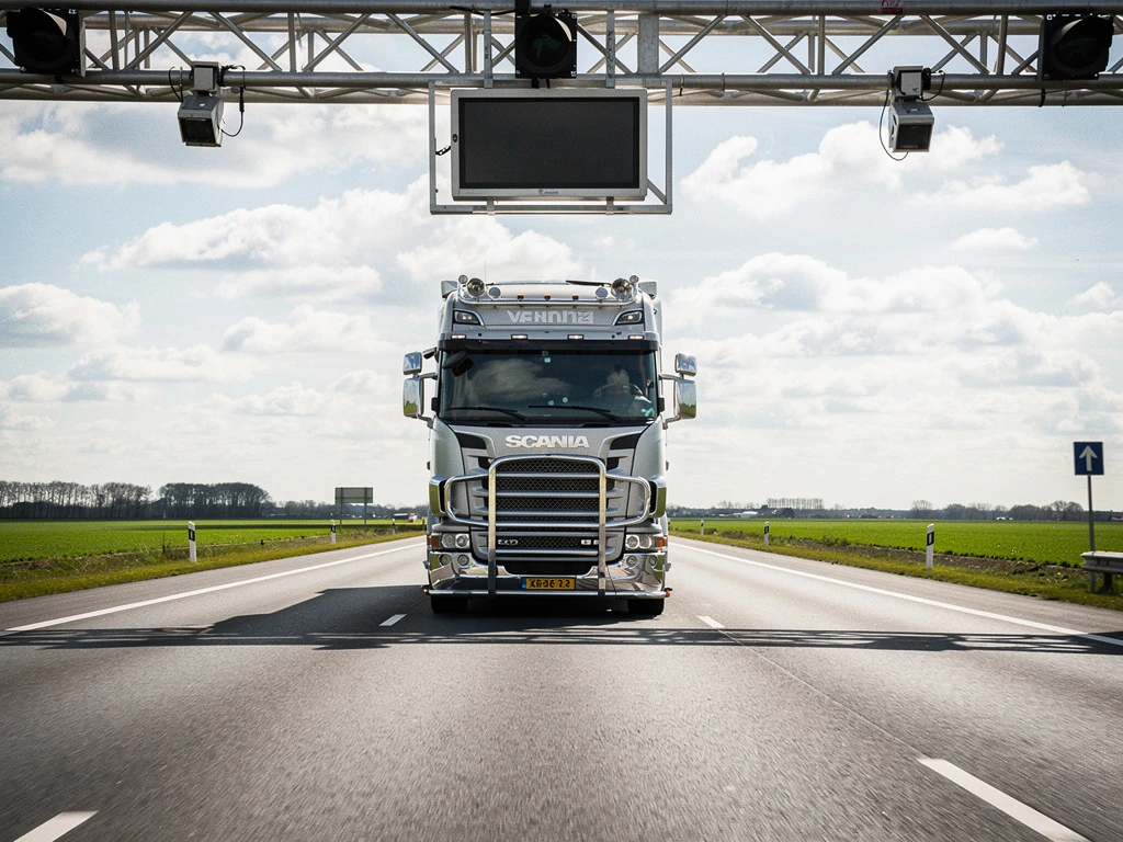 Moderne vrachtwagen rijdt onder elektronische tolpoortry op Nederlandse snelweg met sensoren en camera's zichtbaar